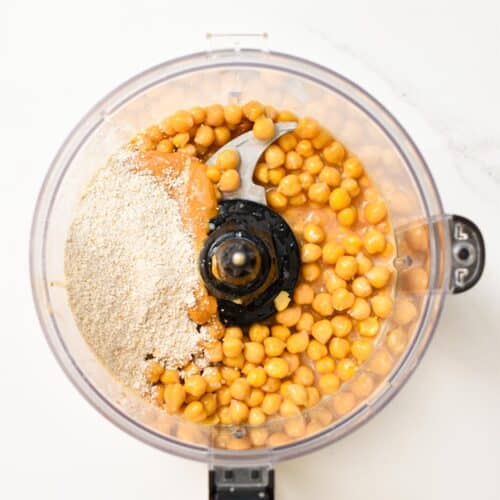 a food processor bowl picture from the top filled with chickpeas, oat flour, maple syrup, vanilla extract, and peanut butter