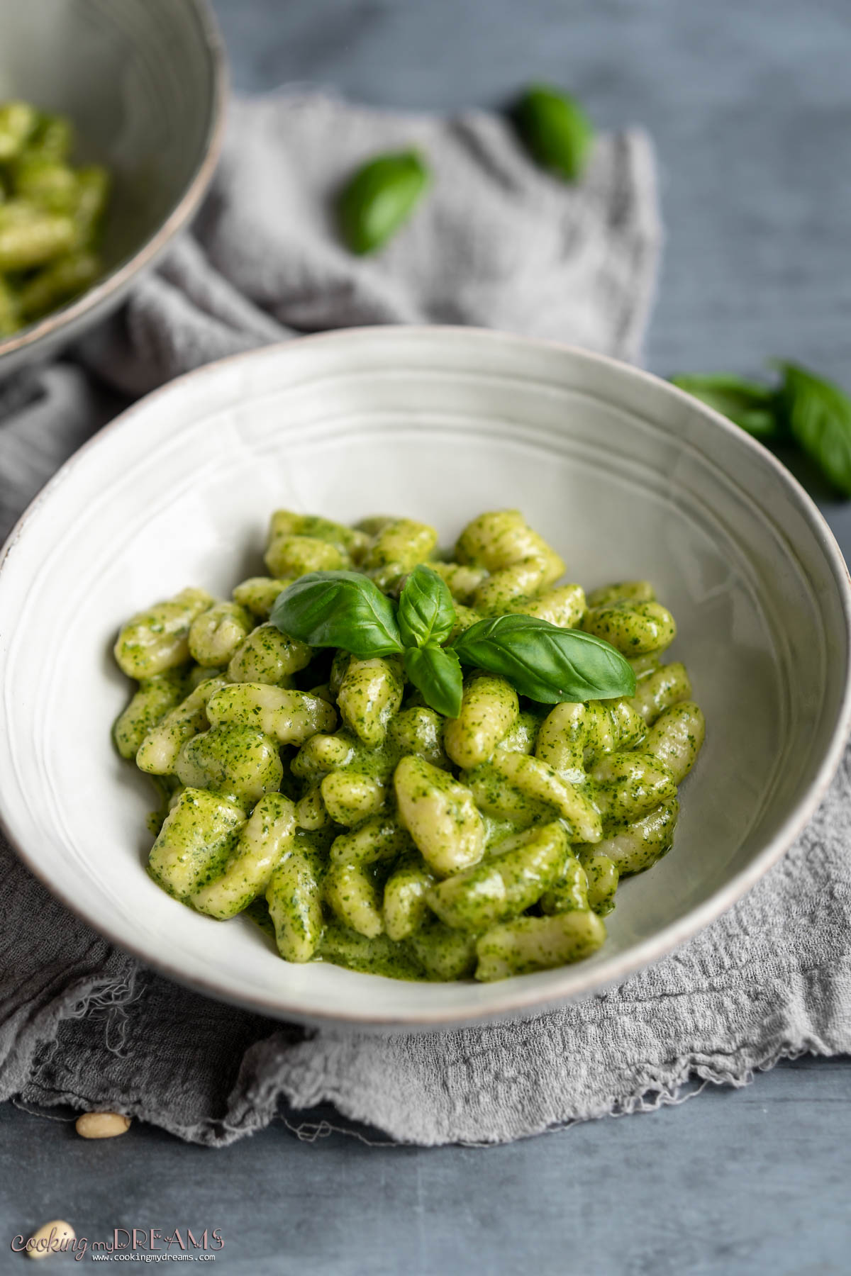 White bowl with creamy pesto gnocchi topped with fresh basil leaves