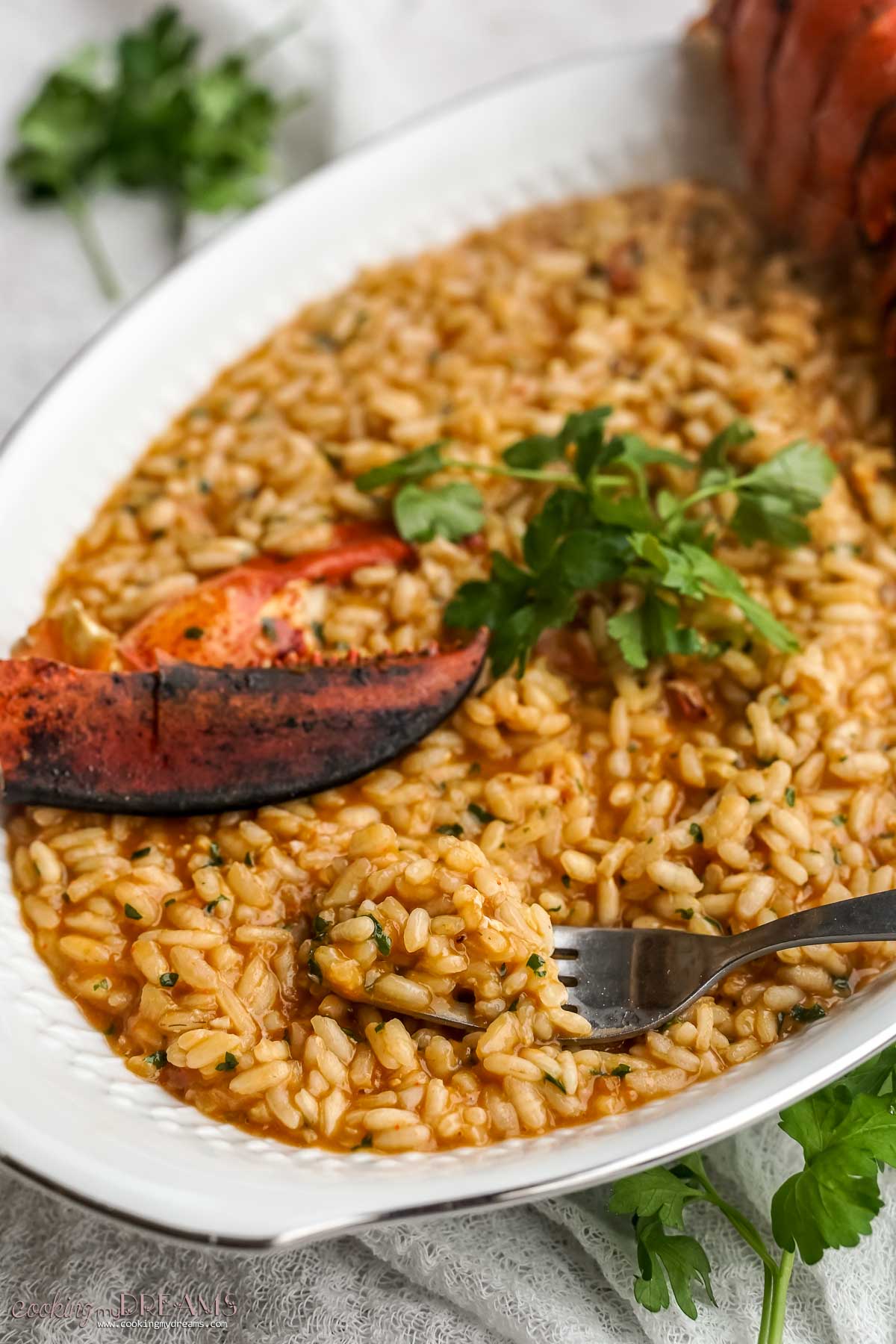 fork digging lobster risotto in a serving tray.